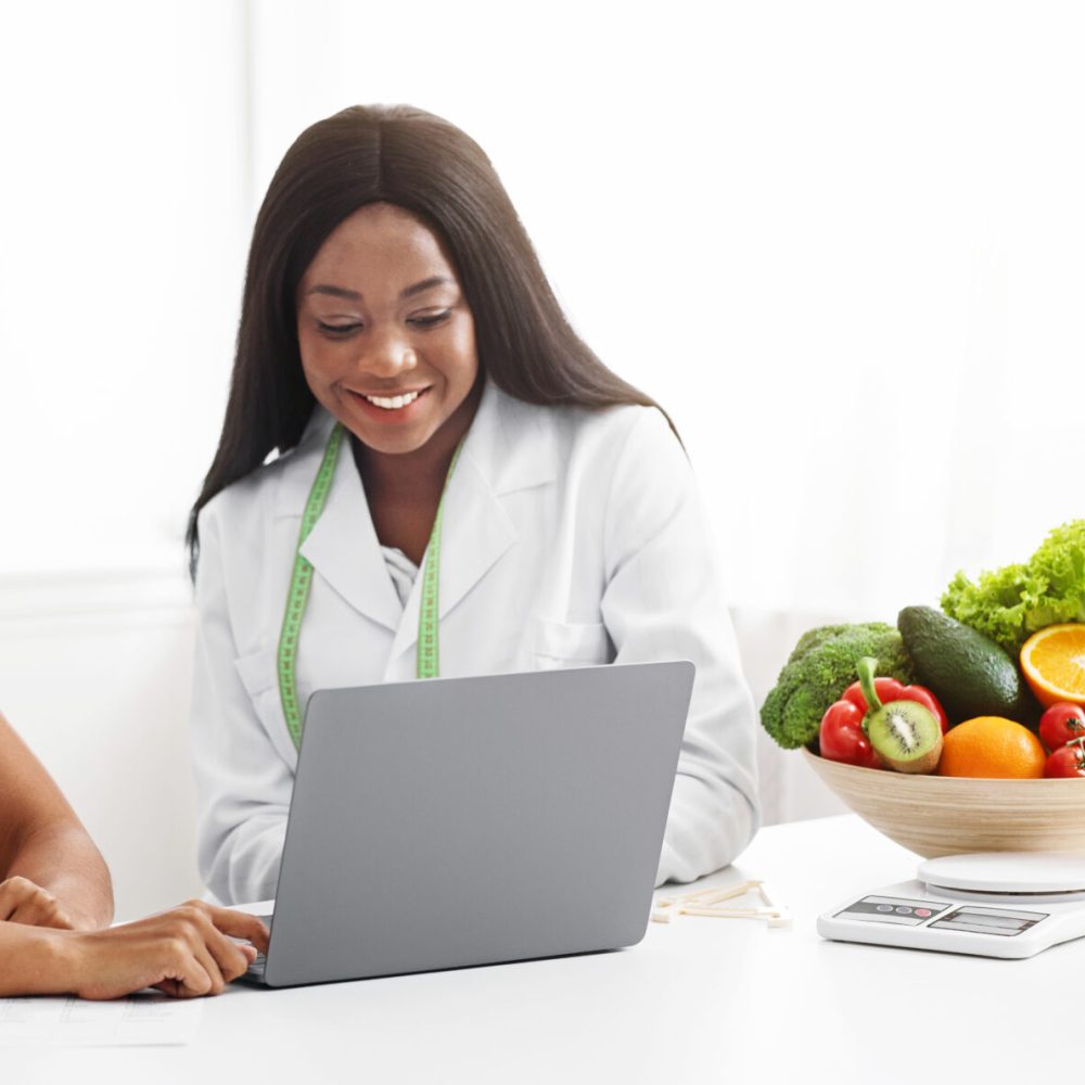 Black women nutritionist and patient looking at laptop screen at clinic, making diet plan, copy space